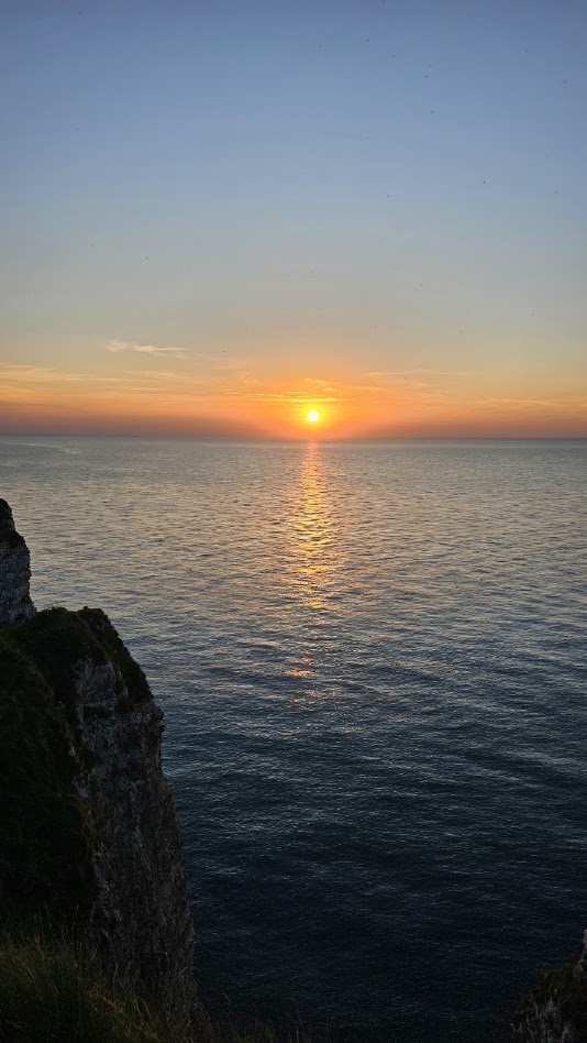 Pôr do sol visto das falésias de Étretat, com o oceano iluminado pela luz dourada do final da tarde.